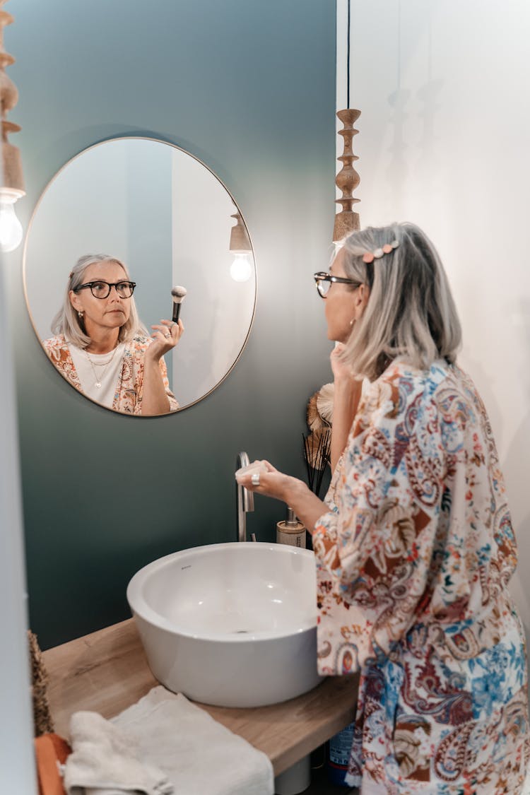 Elderly Woman Looking In Mirror In Bathroom Doing Makeup