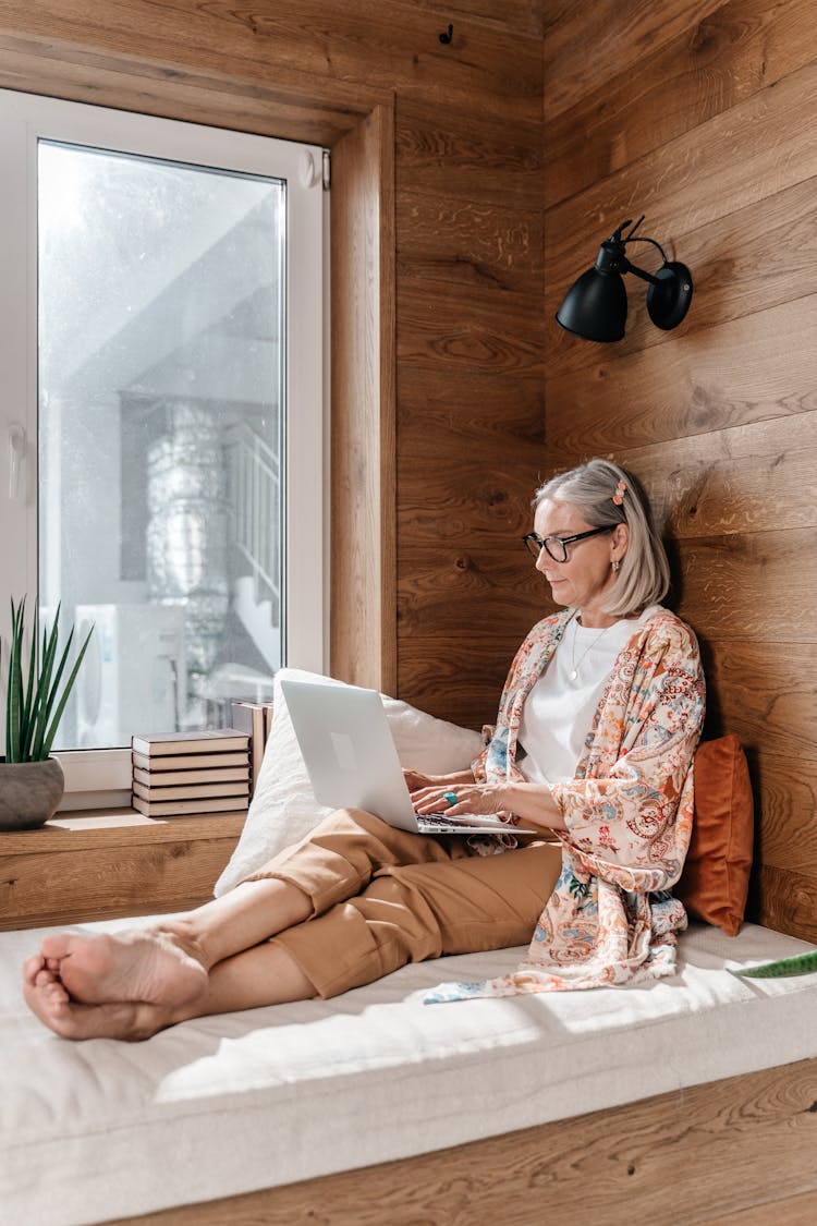 Senior Woman Using Laptop On A Bed In A Wooden Room