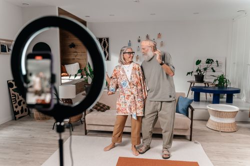 Free A joyful senior couple dances at home while recording with a smartphone. Modern and lively scene. Stock Photo