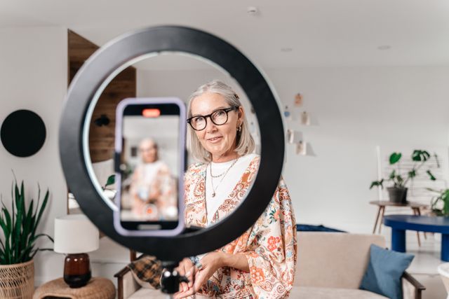 A woman recording a lesson at home with a phone and a ring light