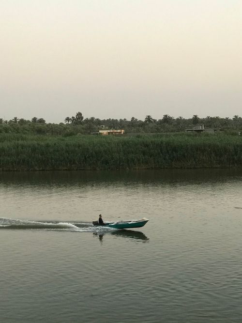 Free A lone person sailing a small boat on a tranquil river at dawn, surrounded by lush greenery. Stock Photo