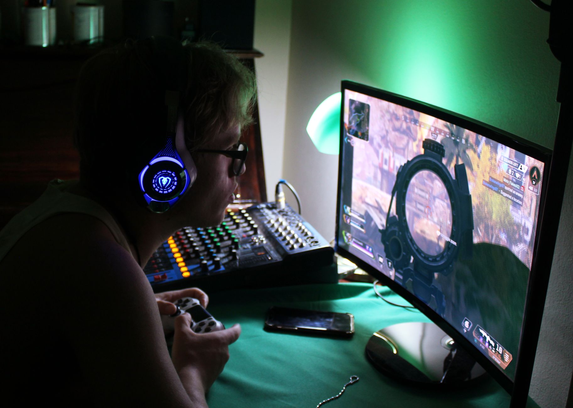 A dedicated gamer using a headset and controller while engrossed in a game, illuminated by green lights.
