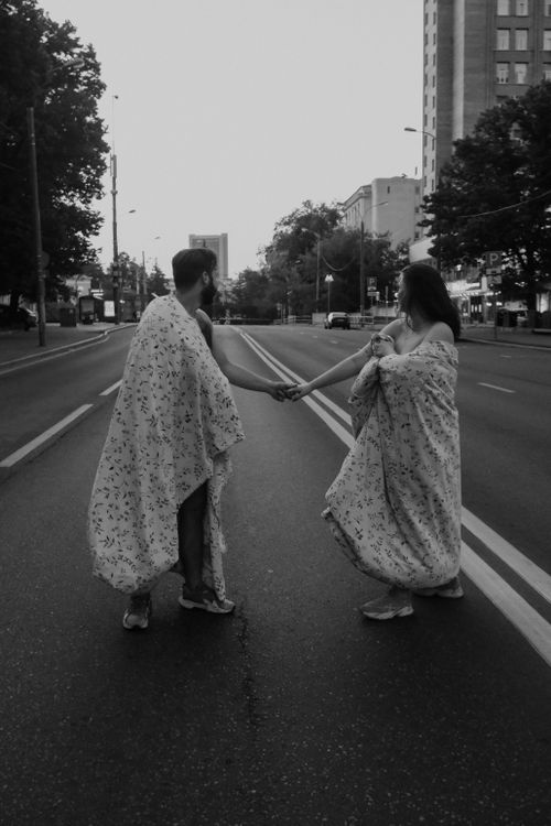 Free Couple wrapped in blankets holding hands on a deserted city street, expressing love and connection. Stock Photo