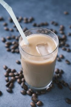 A cool iced coffee in a clear glass surrounded by coffee beans with a straw for sipping.