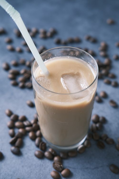Free A cool iced coffee in a clear glass surrounded by coffee beans with a straw for sipping. Stock Photo