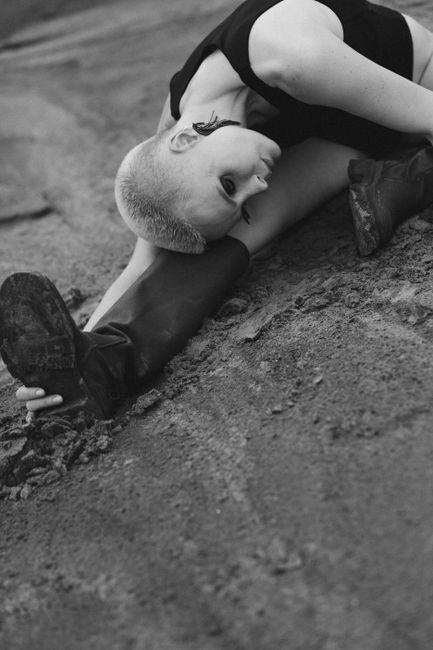 Black and white portrait of a woman stretching on rough ground, displaying artistic expression.