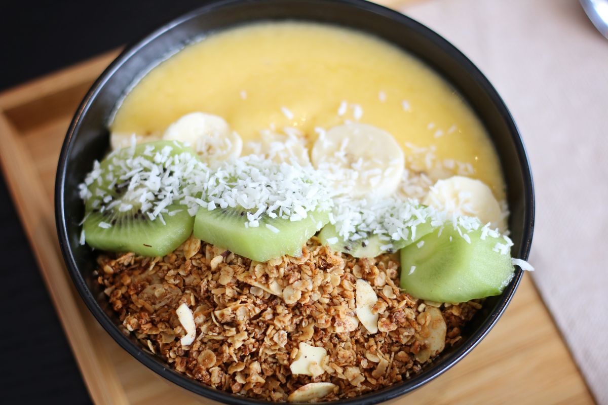 Mango smoothie bowl with banana slices, kiwi chunks, shredded coconut and almond granola