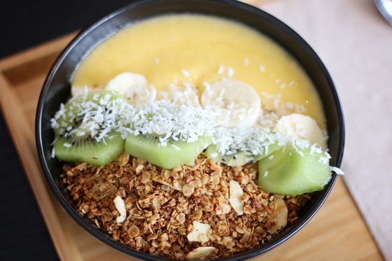 Mango smoothie bowl with banana slices, kiwi chunks, shredded coconut and almond granola