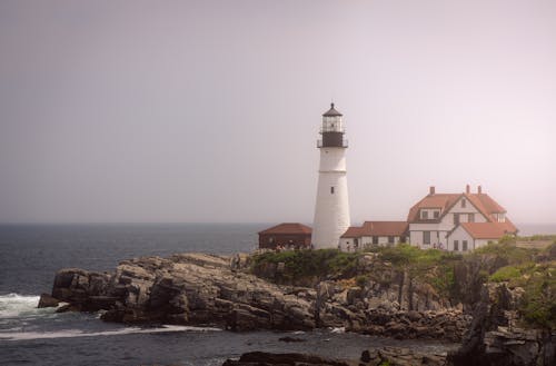 Free Lighthouse and Houses on Island Near Body of Water Stock Photo