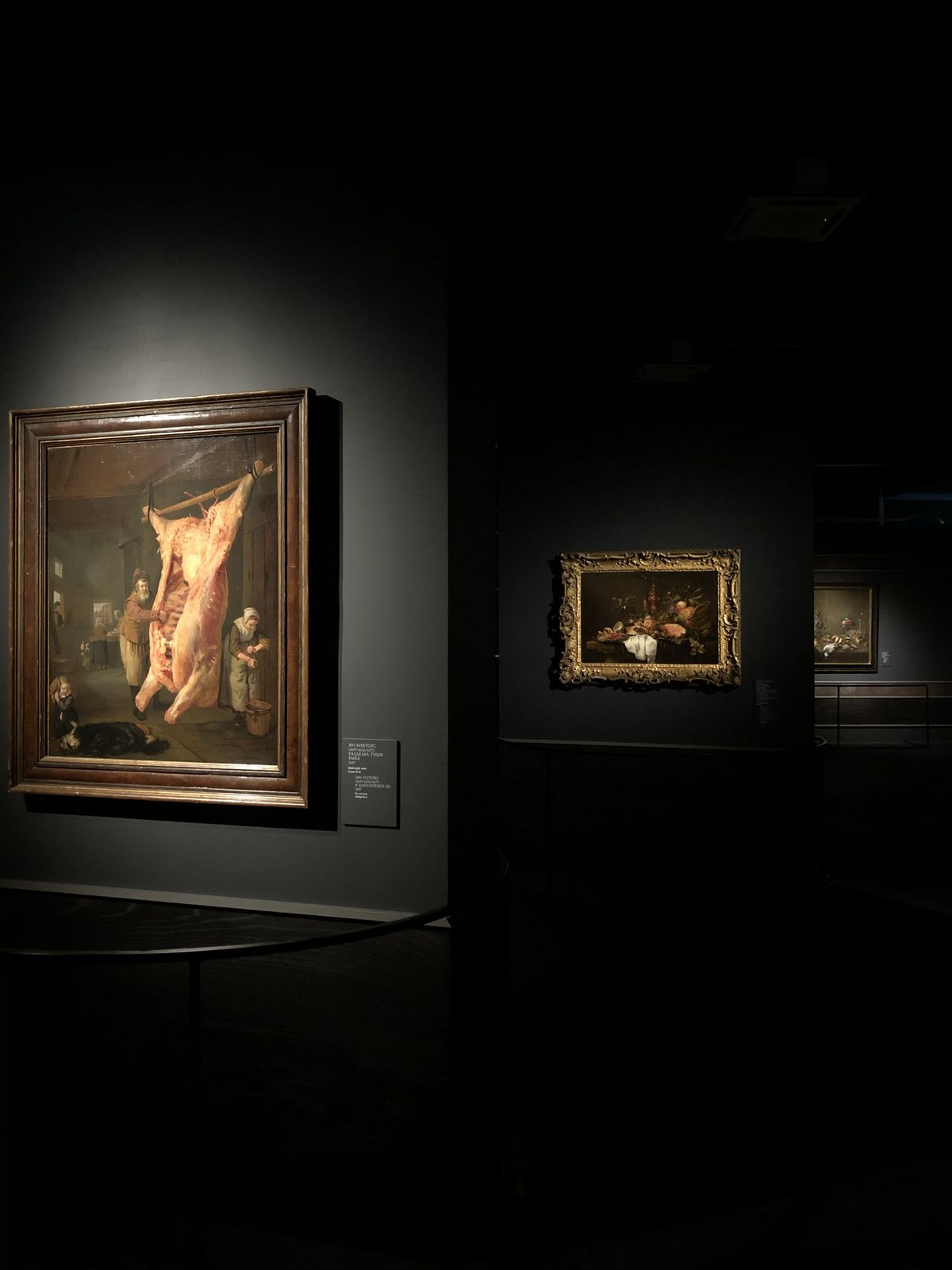 Visitors among old-master paintings on dark gallery walls