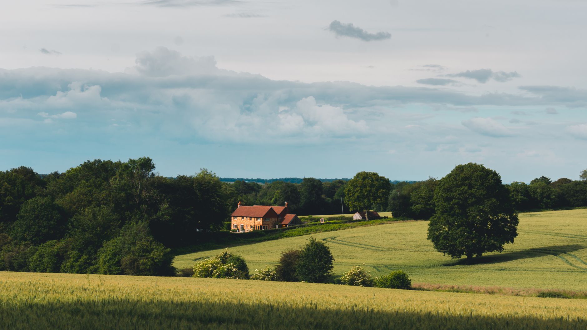 Scenic view of a countryside home surrounded by lush fields and trees under a cloudy sky.