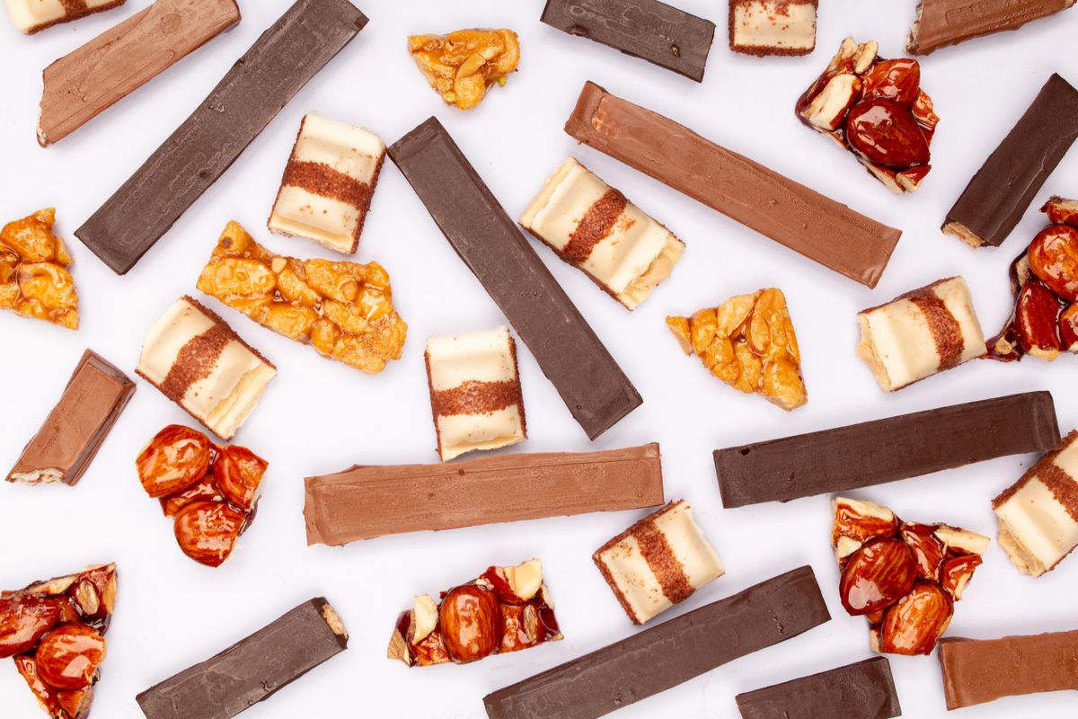 Flat lay of assorted chocolate and nut candy bars on a white surface, showcasing variety and texture.