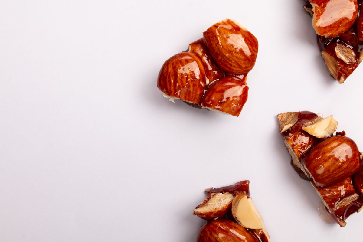 Top view of sweet and crunchy almond brittle pieces on a white background, perfect for food presentations.