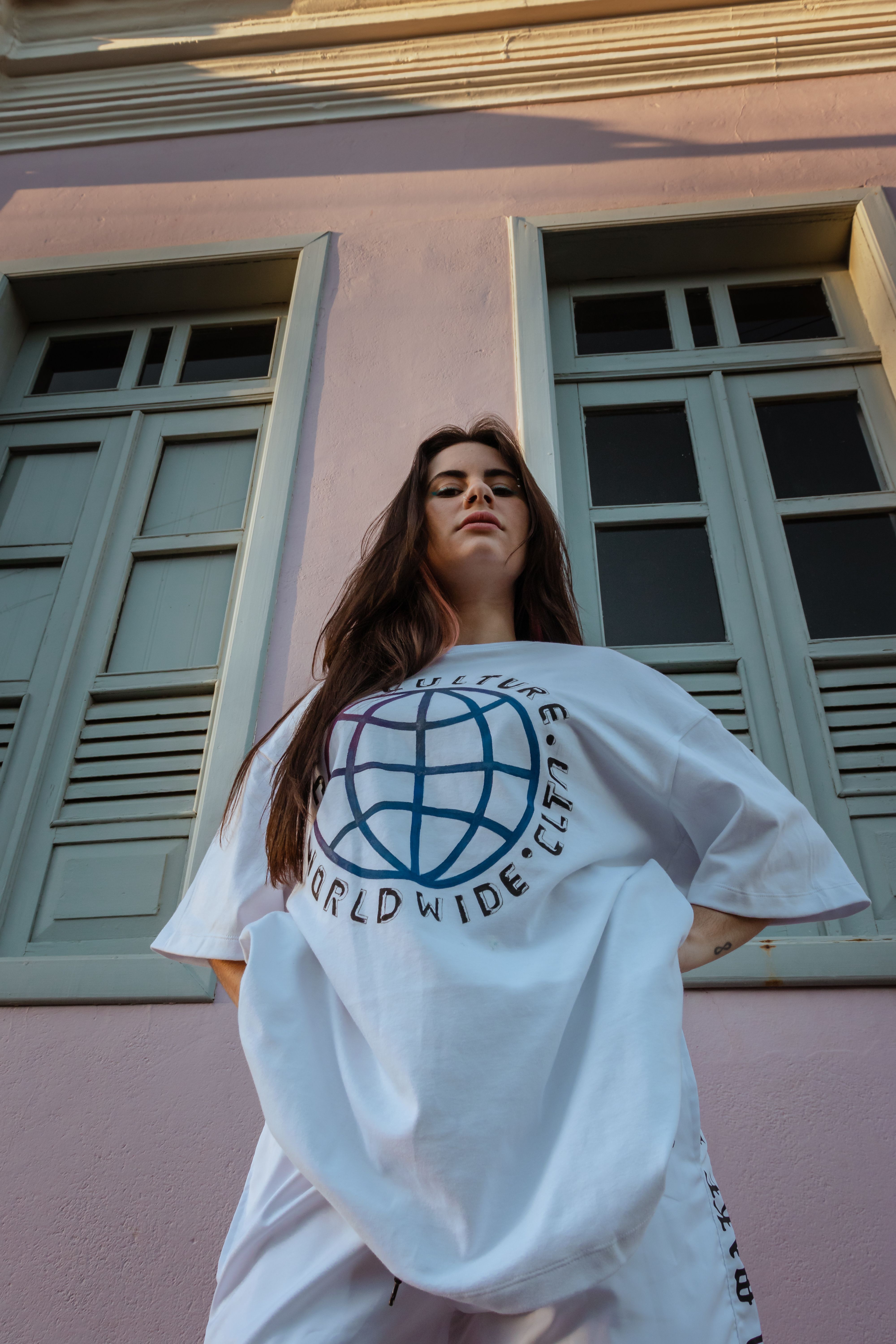 Stylish woman in a white t-shirt posing against pastel building background.