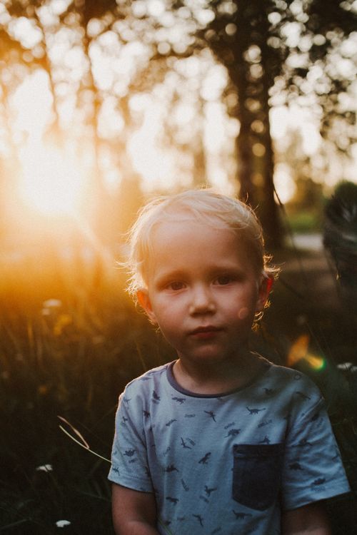 Free A child in a blue shirt stands outdoors at sunset, capturing innocence and warmth. Stock Photo