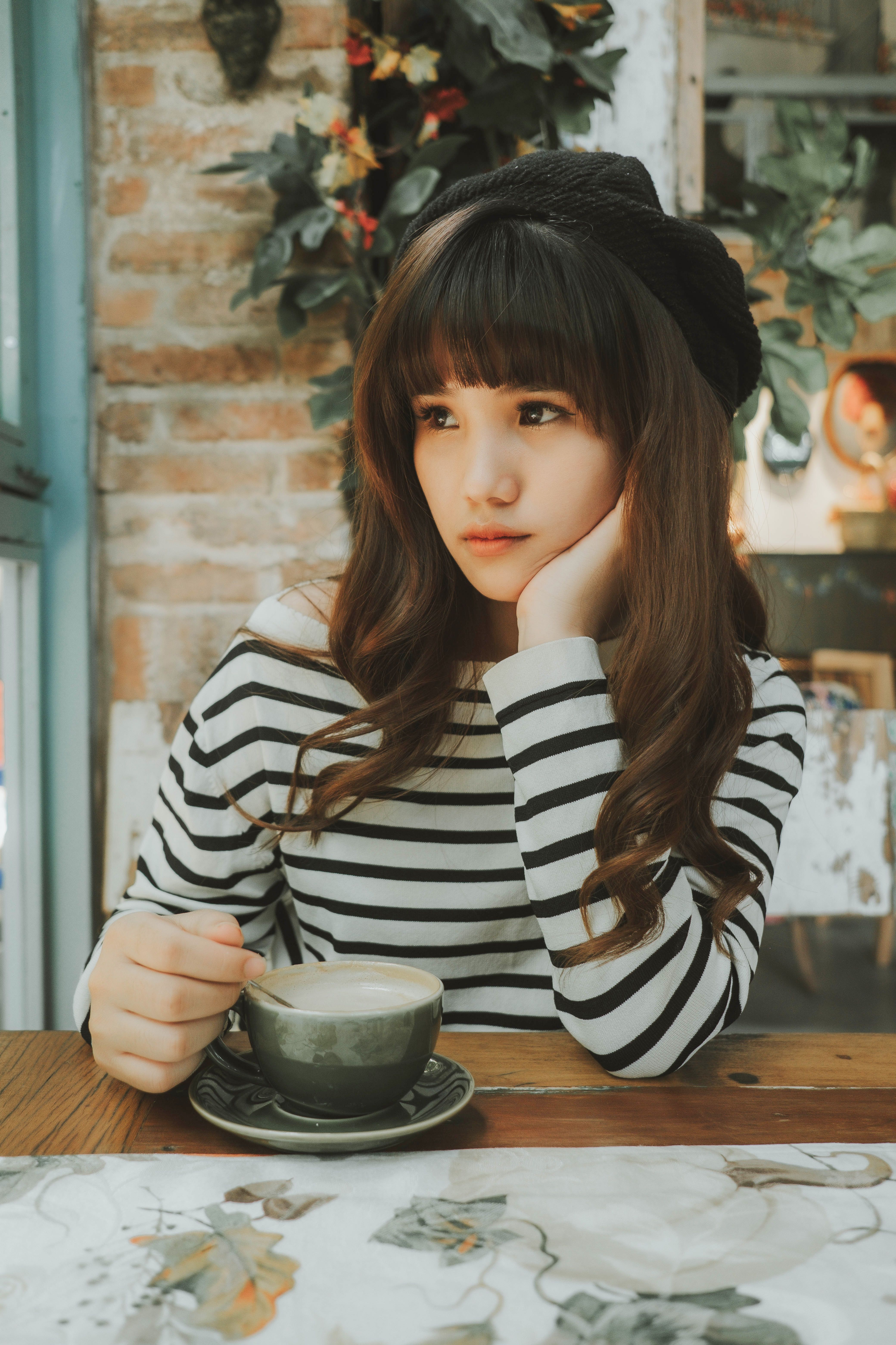 Young woman in striped sweater savoring coffee indoors. Cozy, stylish ambiance.