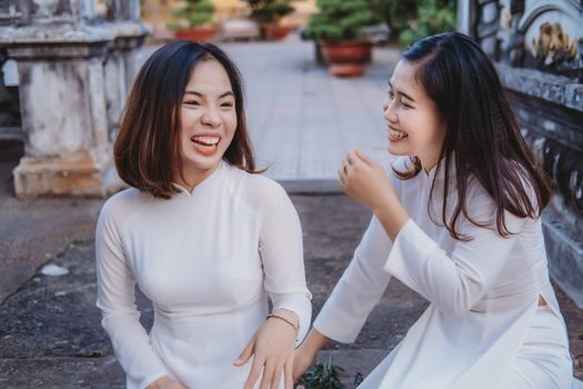 Two Vietnamese women in traditional attire laughing and enjoying a joyful moment outdoors.