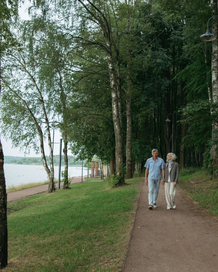 A senior couple walking together along a tree-lined park path.