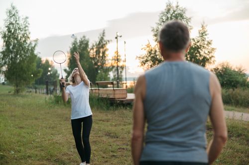 Free A couple enjoying a friendly badminton match on a grassy field during sunset. Stock Photo