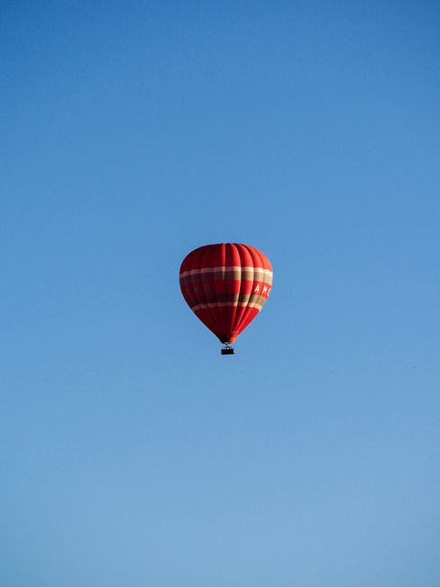 A vibrant red hot air balloon soars high against a bright blue sky, symbolizing freedom and adventure.
