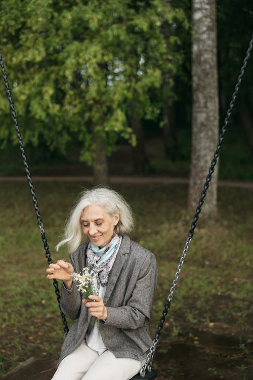 Elderly Woman Sitting on Swing while Holding Flowers