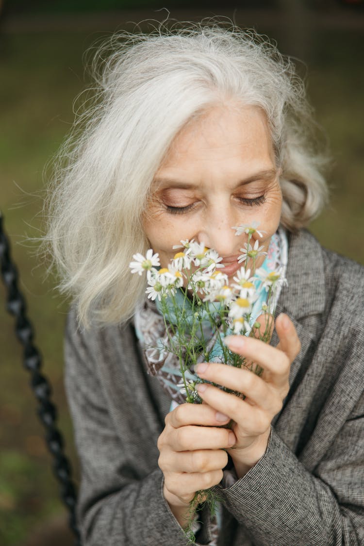 Close-Up Shot Of An Elderly Woman Smelling The White Daisies