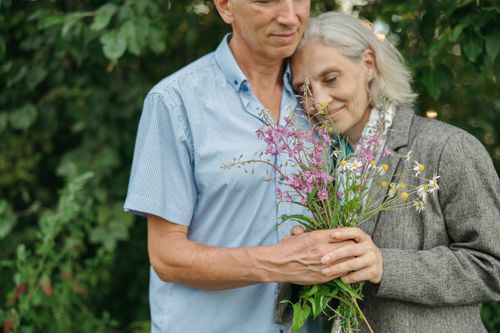 Free Elderly couple sharing a tender moment outdoors holding wildflowers, symbolizing love and companionship. Stock Photo