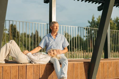 Free Man in Blue Dress Shirt and Brown Pants Sitting on Brown Wooden Bench Stock Photo