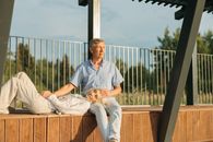 Man in Blue Dress Shirt and Brown Pants Sitting on Brown Wooden Bench