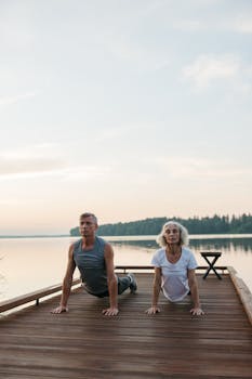 Elderly couple performing yoga outdoors by a serene lake.