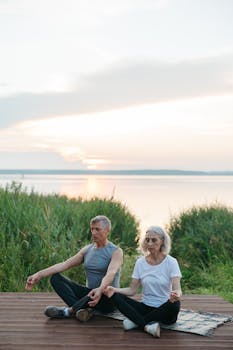 Elderly couple practicing mindfulness and meditation by the lake during sunrise.