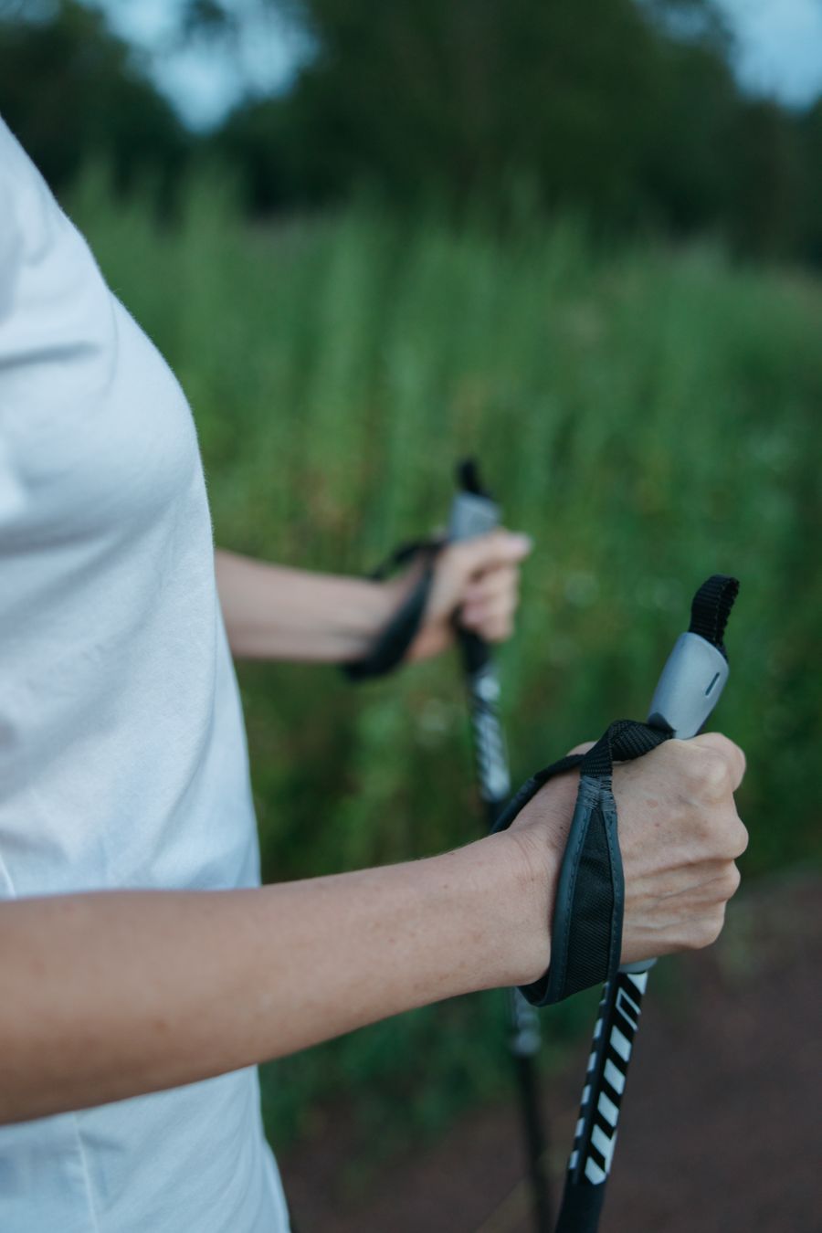Close-up of a woman holding trekking poles, surrounded by lush greenery, outdoors. Stock Photo