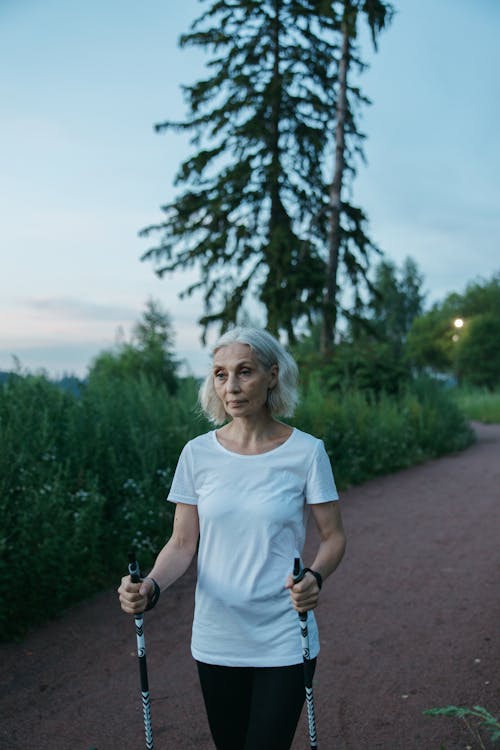 Elderly Woman in White Shirt Using Walking Sticks