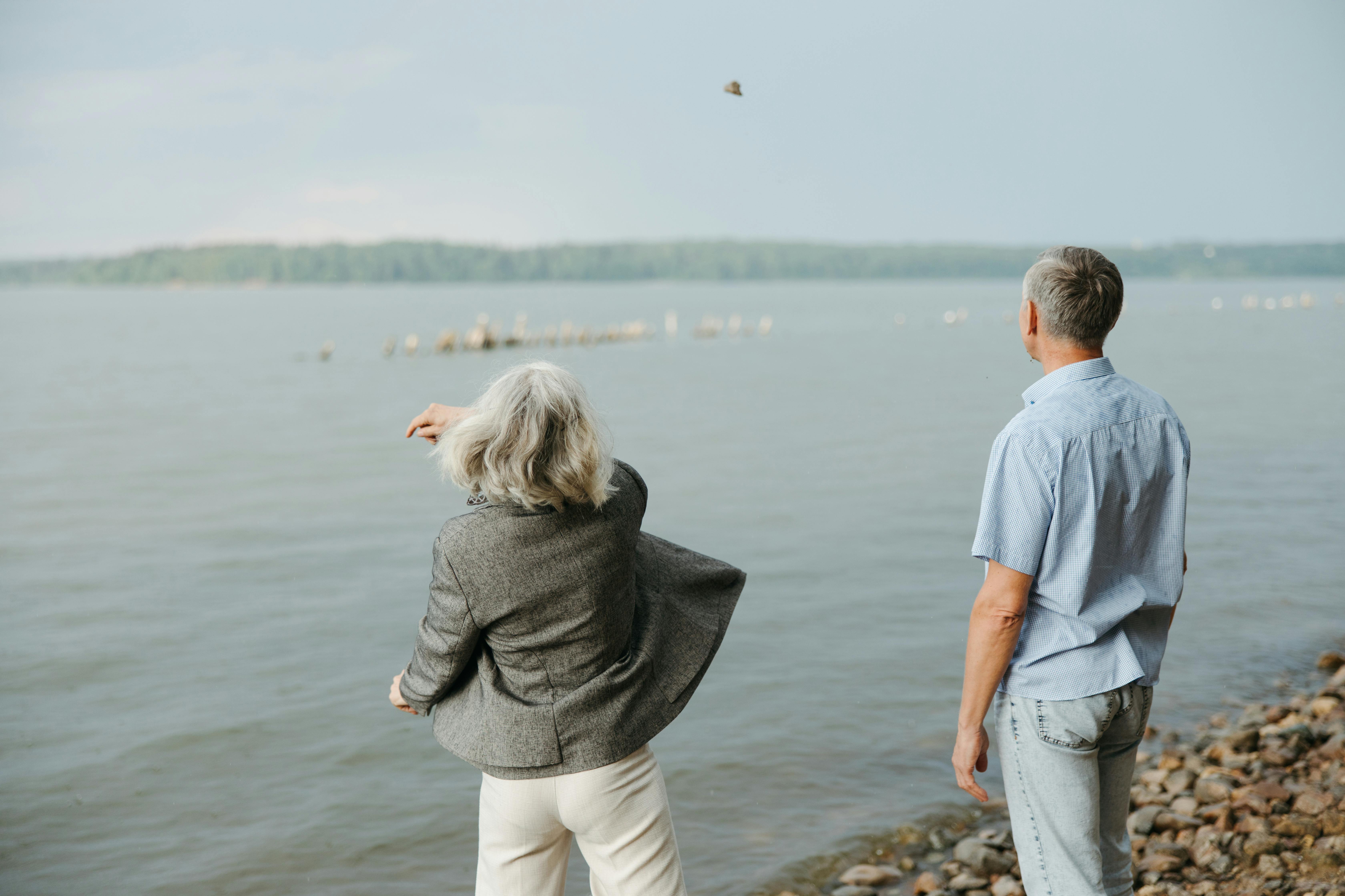 Elderly couple by the lake, enjoying serene nature. Back view, peaceful setting.