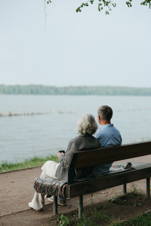 Free Senior couple sitting on a bench, enjoying a peaceful view by the lake. Stock Photo