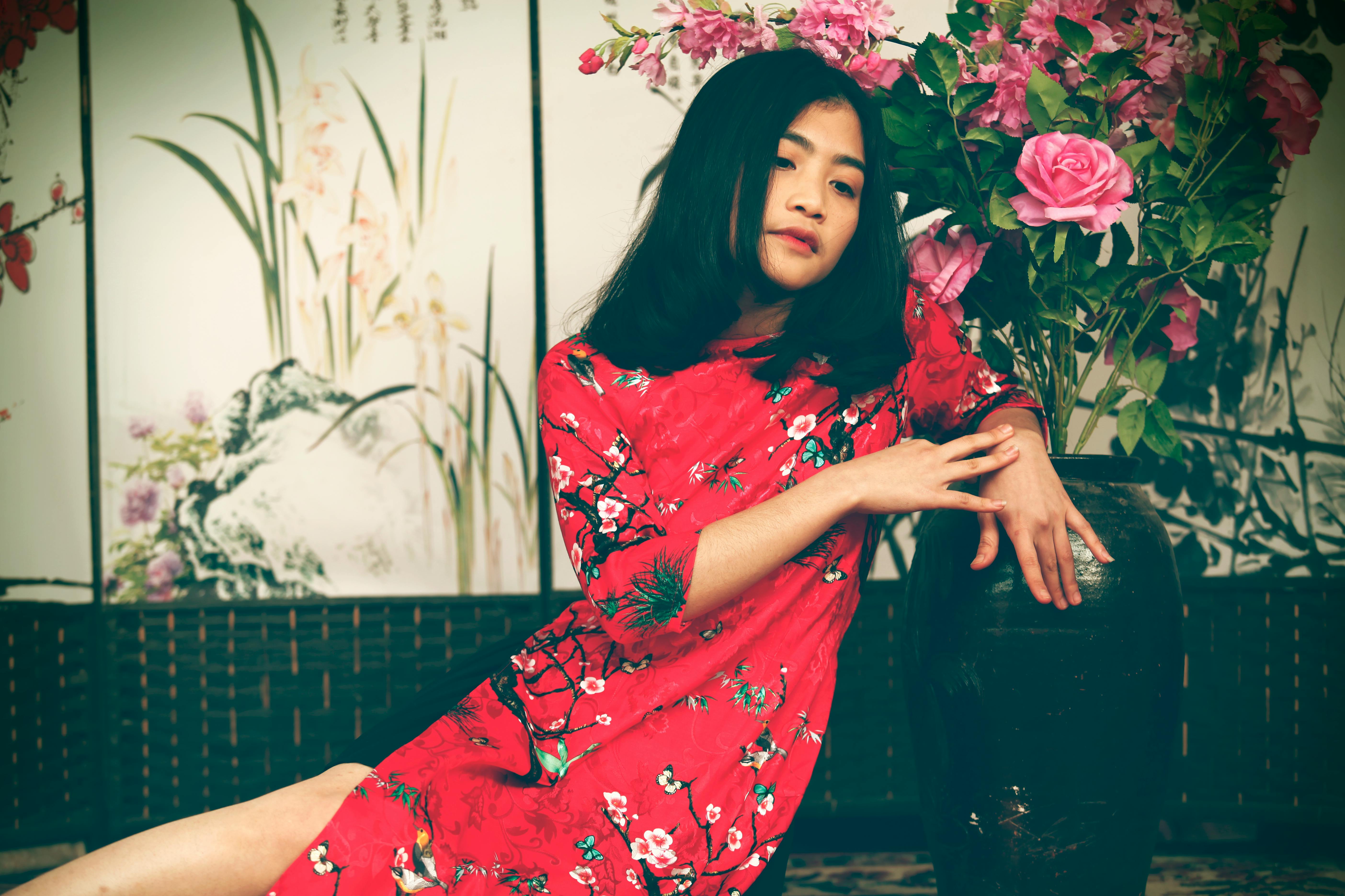 Asian woman posing gracefully in a red floral kimono indoors, surrounded by artistic decor.