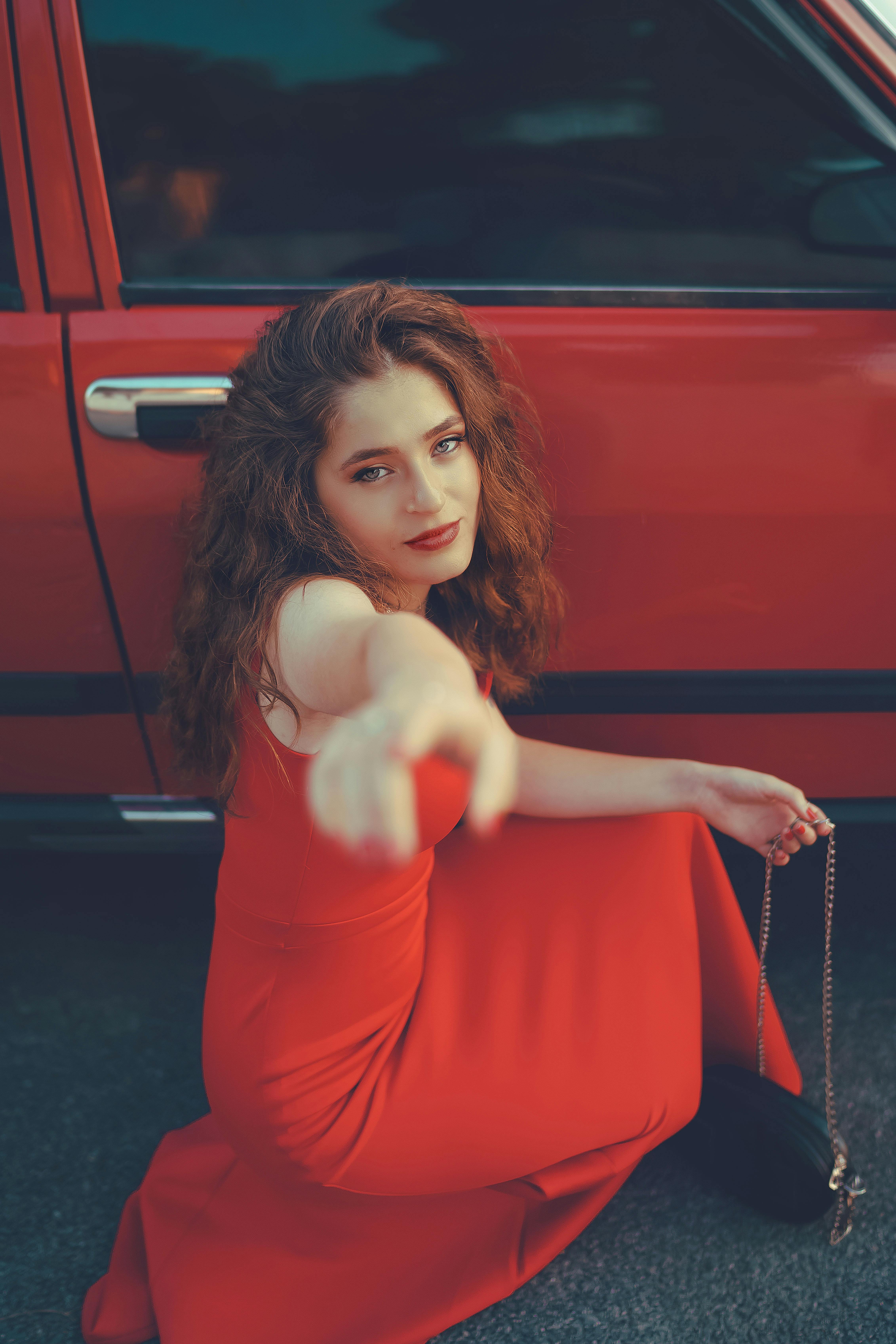 Woman in Red Sleeveless Dress Sitting Against a Car Door  Free Stock Photo
