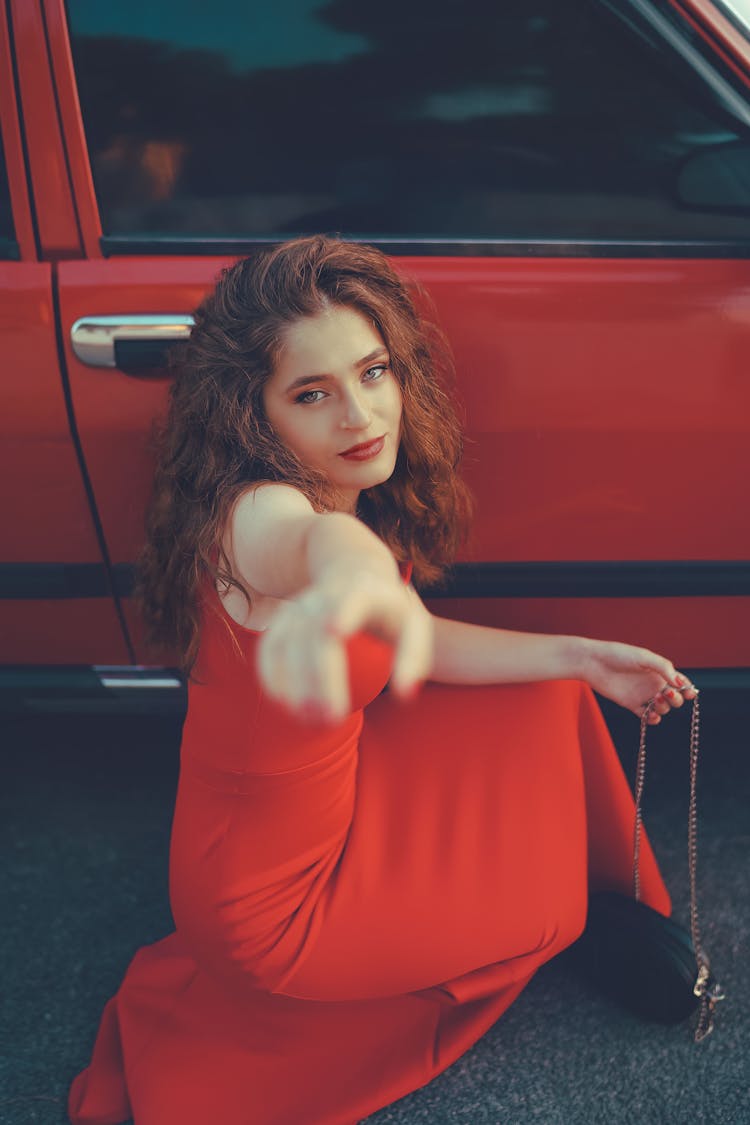 Woman In Red Sleeveless Dress Sitting Against A Car Door
