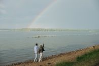 Man and Woman Walking on Brown Sand Near Body of Water