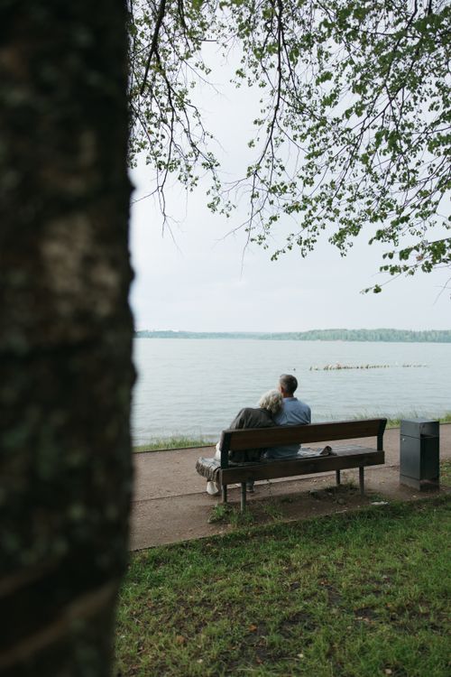 Free Elderly couple sitting on a park bench by a serene lake, embracing love and tranquility. Stock Photo