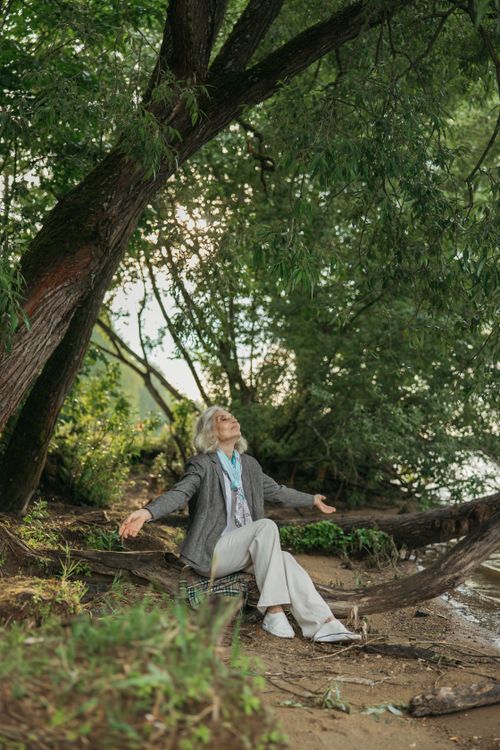 Free Elderly woman seated under a tree, embracing nature, showcasing freedom and serenity. Stock Photo