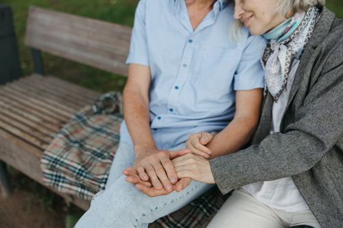 Free A touching moment of an elderly couple holding hands on a park bench symbolizing love and companionship. Stock Photo