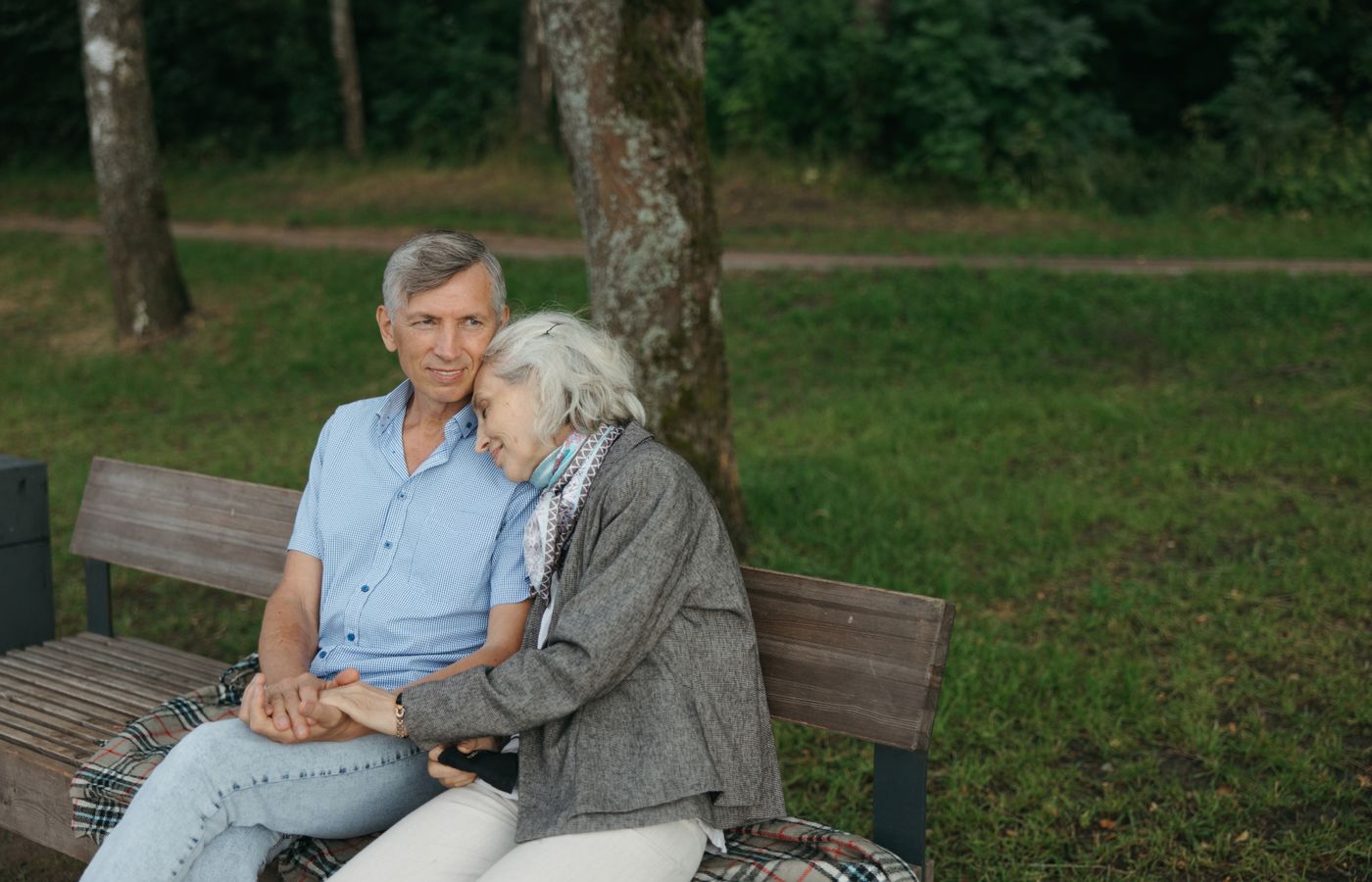 An affectionate elderly couple sitting on a bench in a peaceful park setting, showcasing love and companionship.