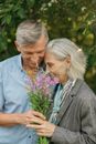 Man in Gray Suit Jacket Beside Woman in Blue Dress Holding Purple Flowers