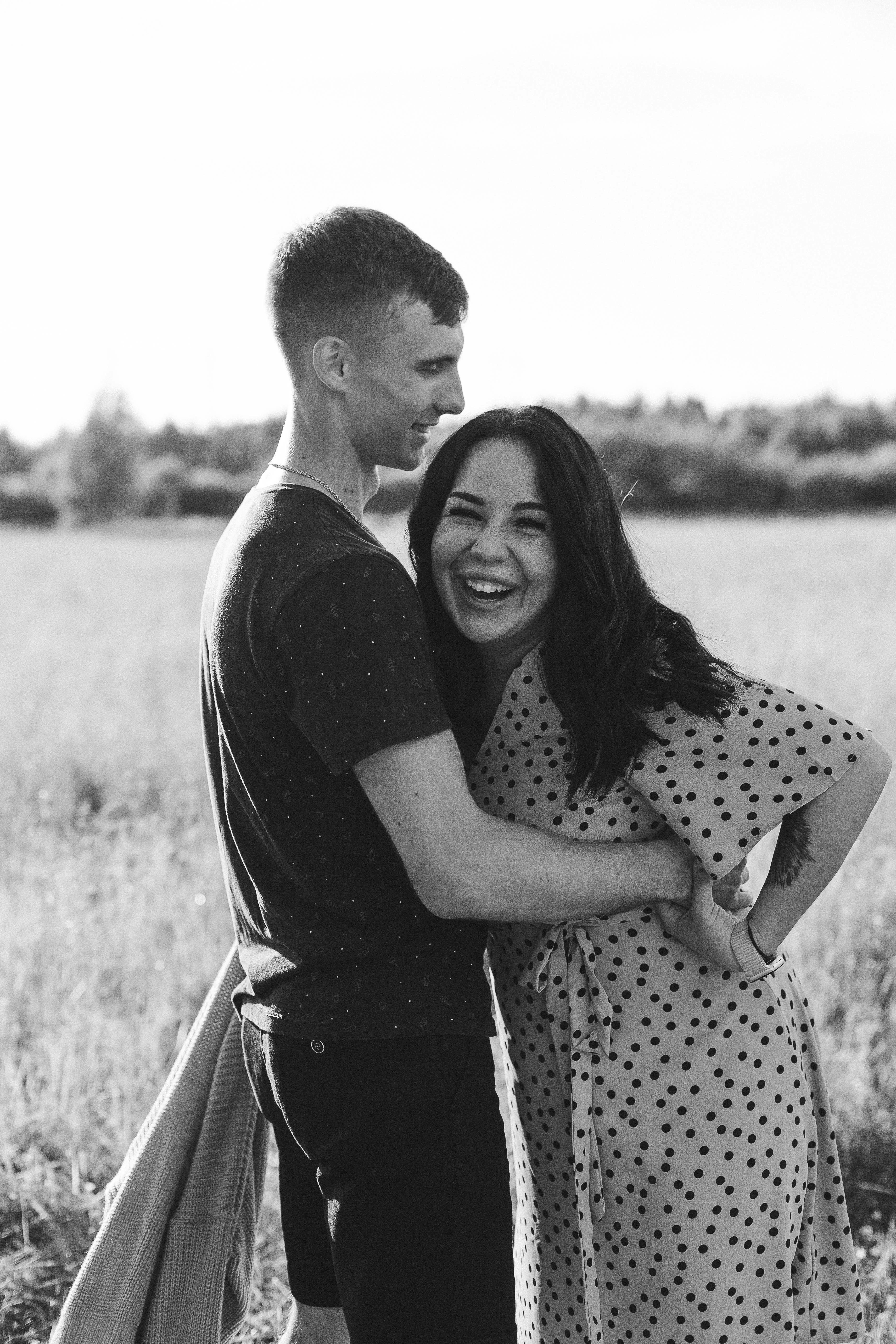 Black and white photo of a couple laughing and embracing in a sunny field.