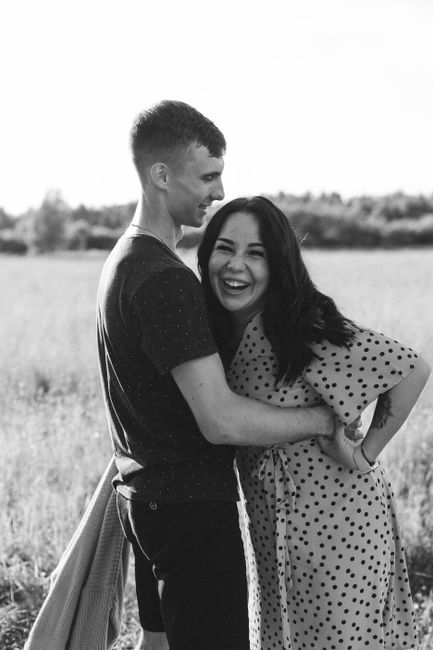 Black and white photo of a couple laughing and embracing in a sunny field.