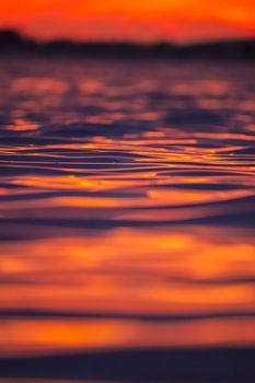 Close-up of vibrant sunset reflecting on a rippling water surface, creating a warm abstract pattern.