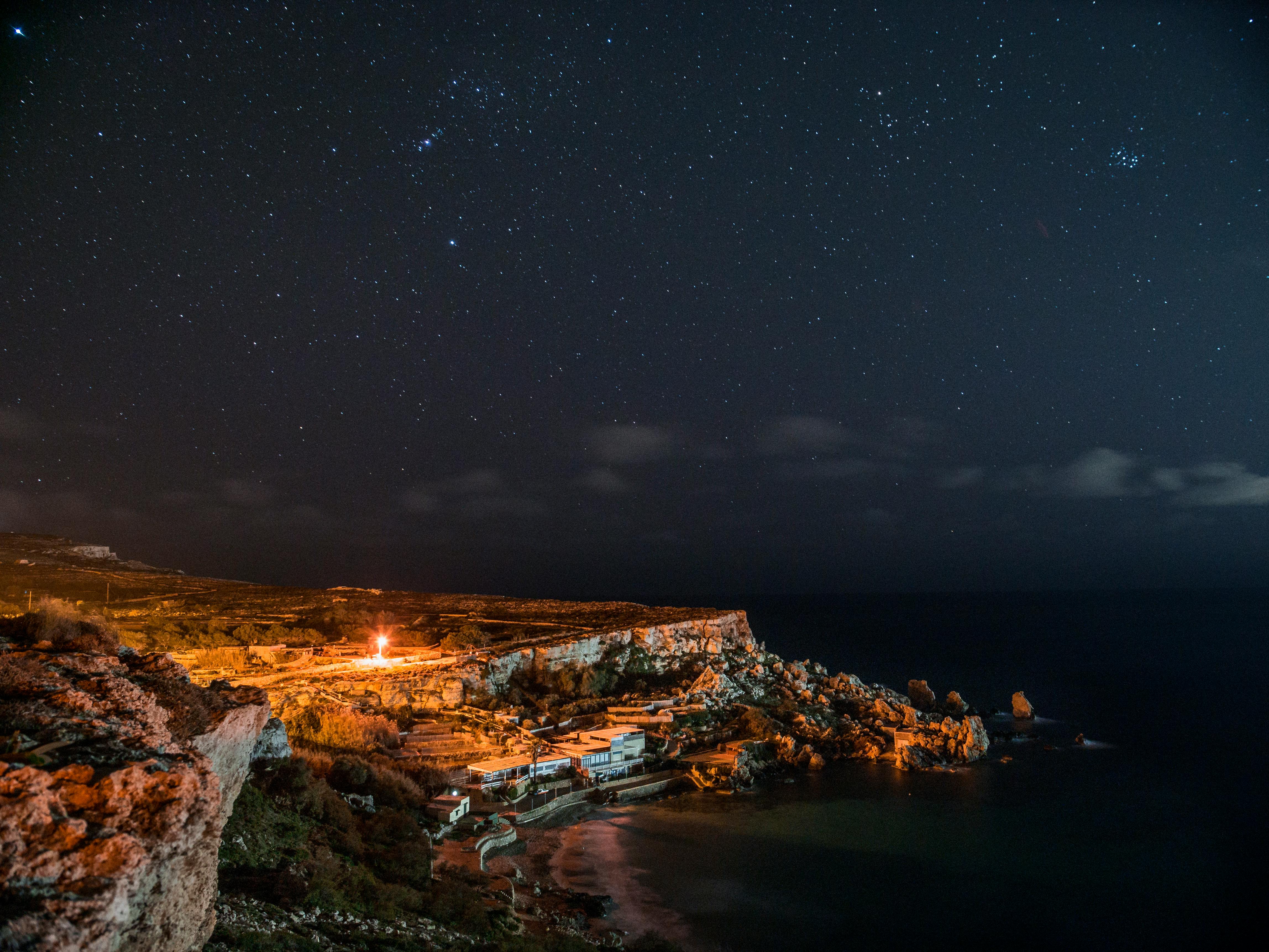 Rock Cliff Near Body of Water Under Clouds and Sky during Nighttime