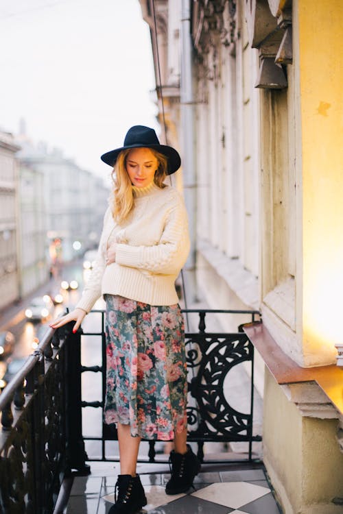 Pregnant Woman Wearing White Sweater and Multicolored Floral Skirt Standing on Balcony