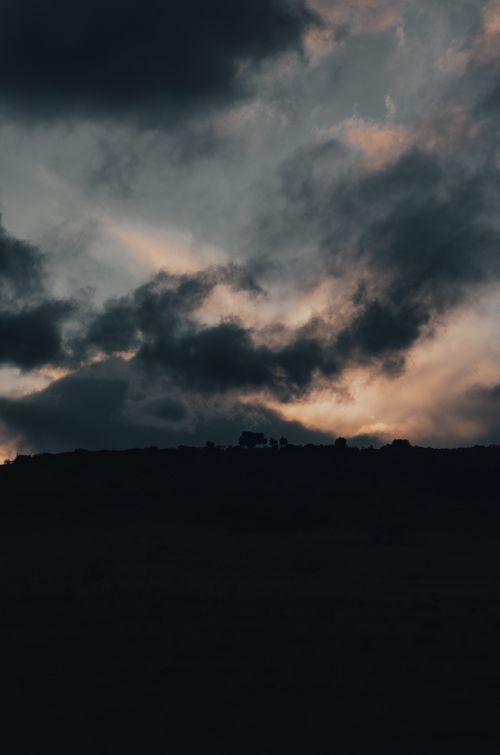 Free Dark clouds over a silhouetted landscape at twilight, capturing the drama of nature. Stock Photo